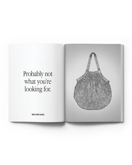Open magazine spread featuring Balenciaga text on the left page and a textured mesh tote bag on the right page against a white backdrop.