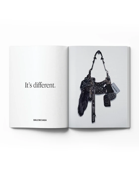 Balenciaga open print catalog spread featuring a black studded handbag adorned with charms next to the text It's different.
