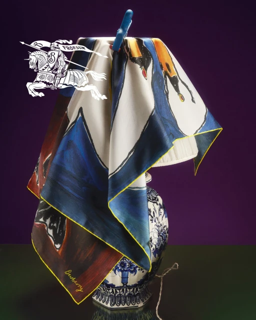 Elegant silk scarf featuring equestrian illustration draped over an ornate blue and white porcelain vase against a deep purple backdrop.