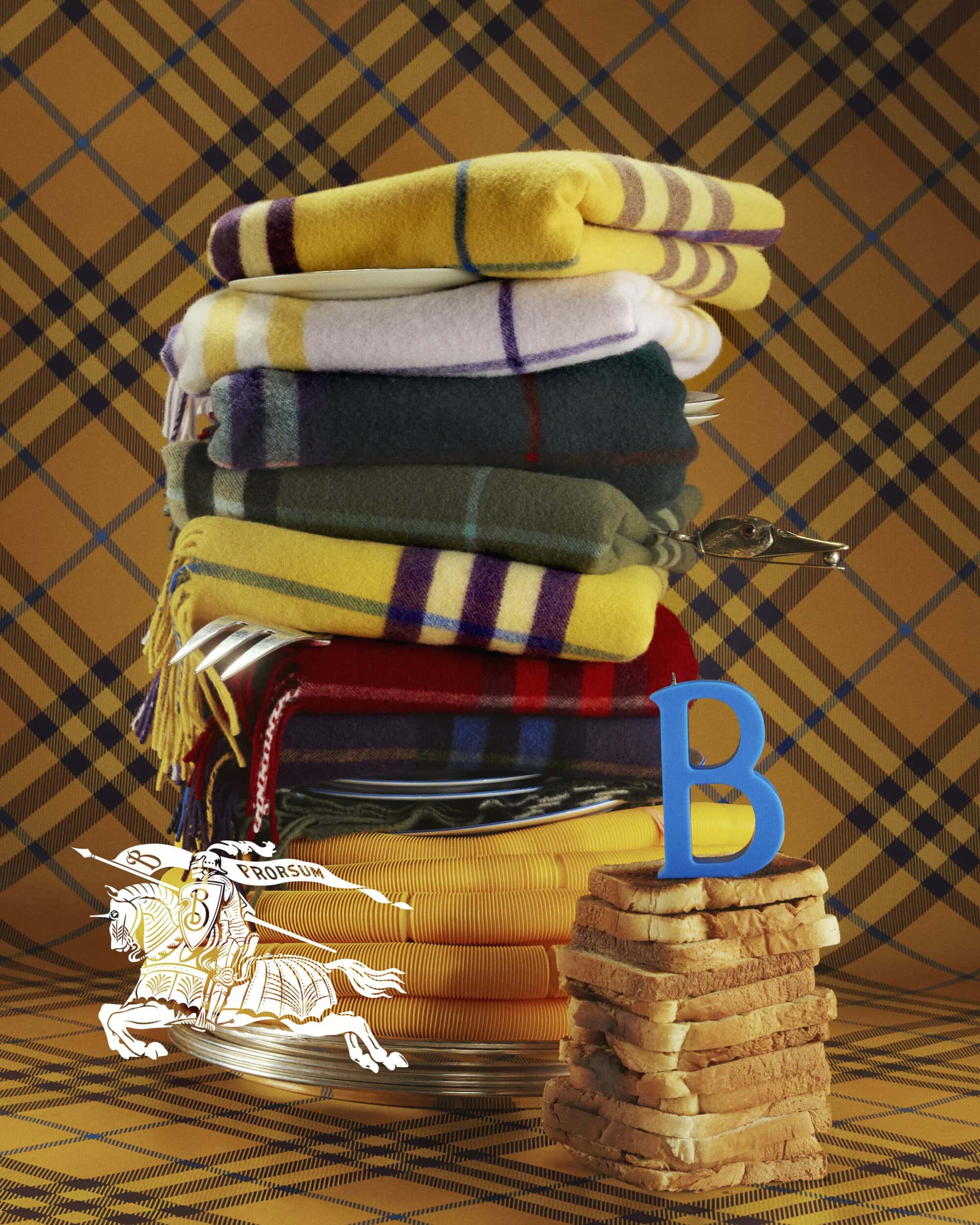 Still life with a stack of folded tartan wool blankets, a stack of toast, and a logo on a tartan fabric backdrop.