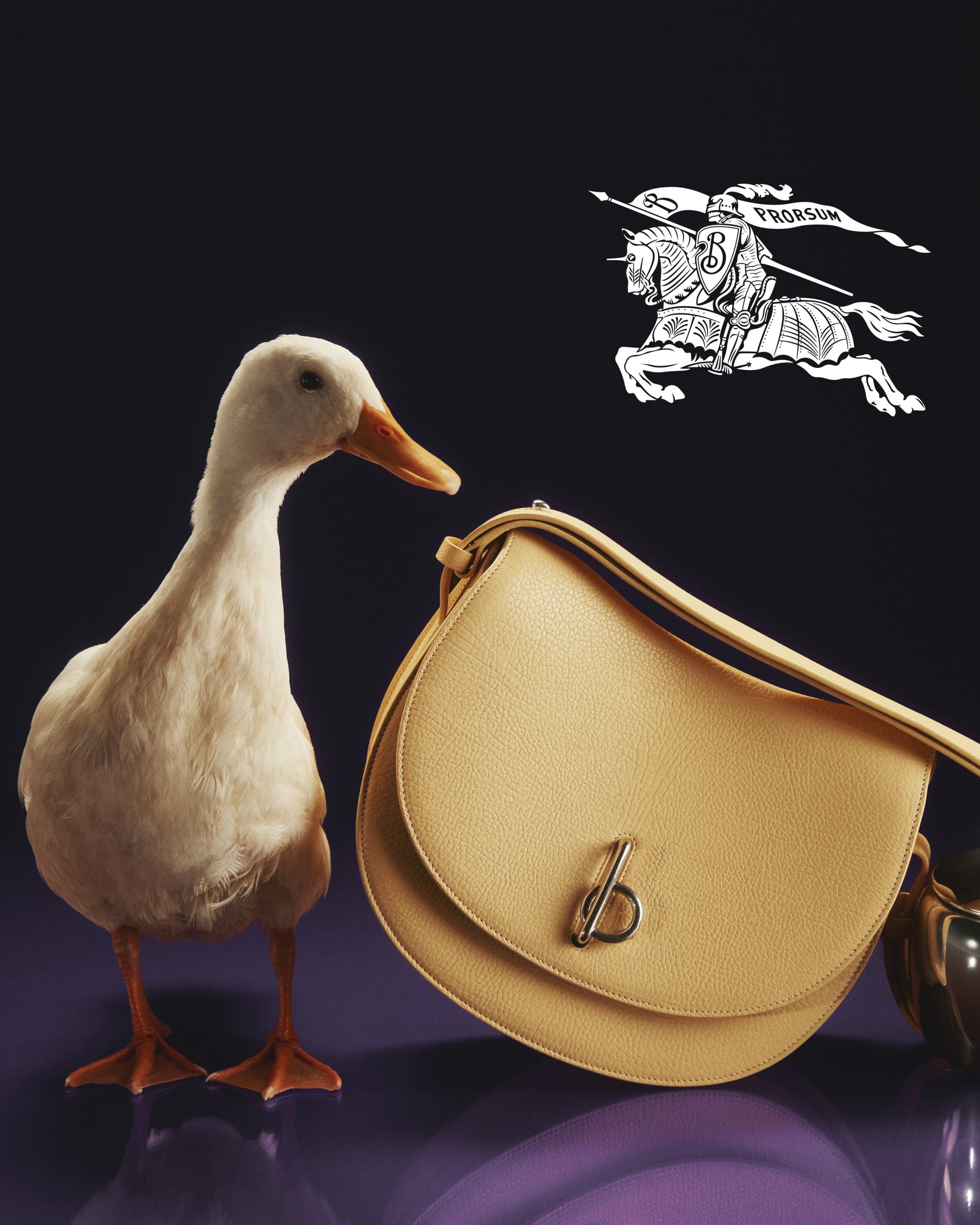 Fashion still life of a beige handbag next to a white duck, set against a dark background with the Burberry logo floating above.