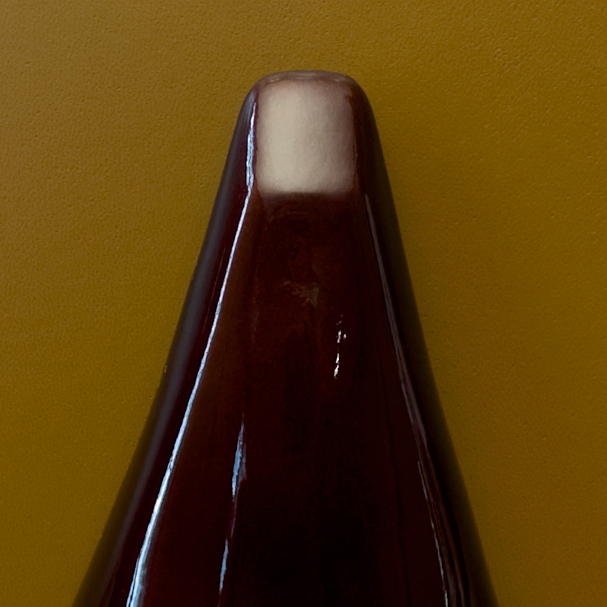 Close-up of a glossy, tapered dark brown object with a light beige top against a solid mustard-yellow background.