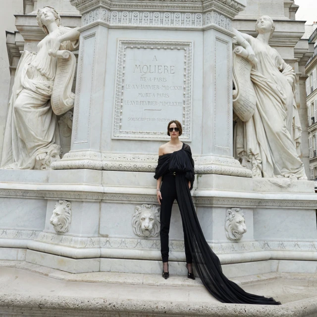Elegant woman in black jumpsuit poses near monument with statues. Parisian urban setting. Fashionable editorial image.