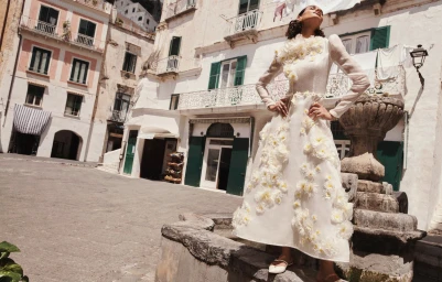 Barbara Valente wearing a white floral appliqué Zimmermann dress while posing on a stone fountain in an Italian town square.