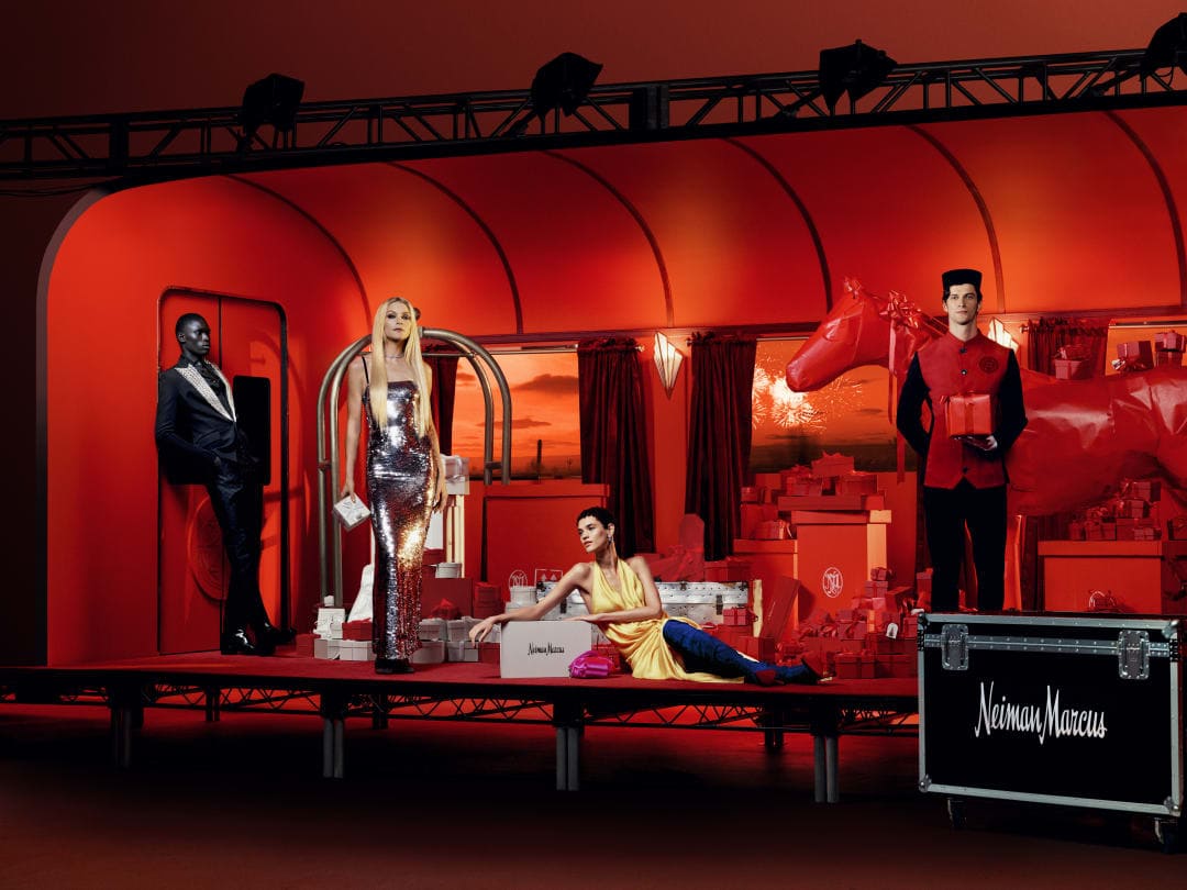 Window display with mannequins in gowns and suits surrounded by gifts in an artificial, monochromatic luxury retail environment.