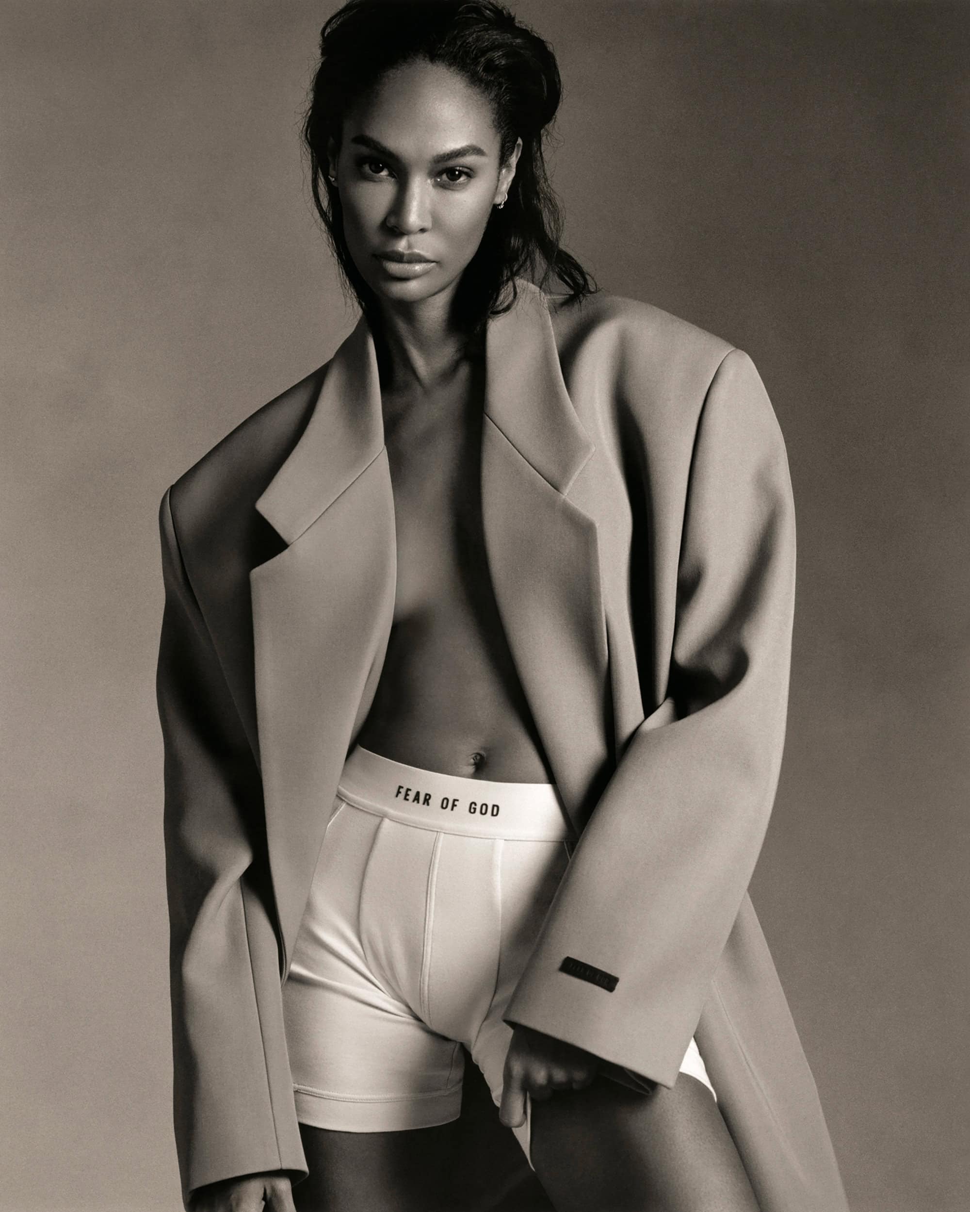 Indoor studio shot of a confident adult female wearing a blazer and underwear, posing against a neutral backdrop, in a fashion editorial.