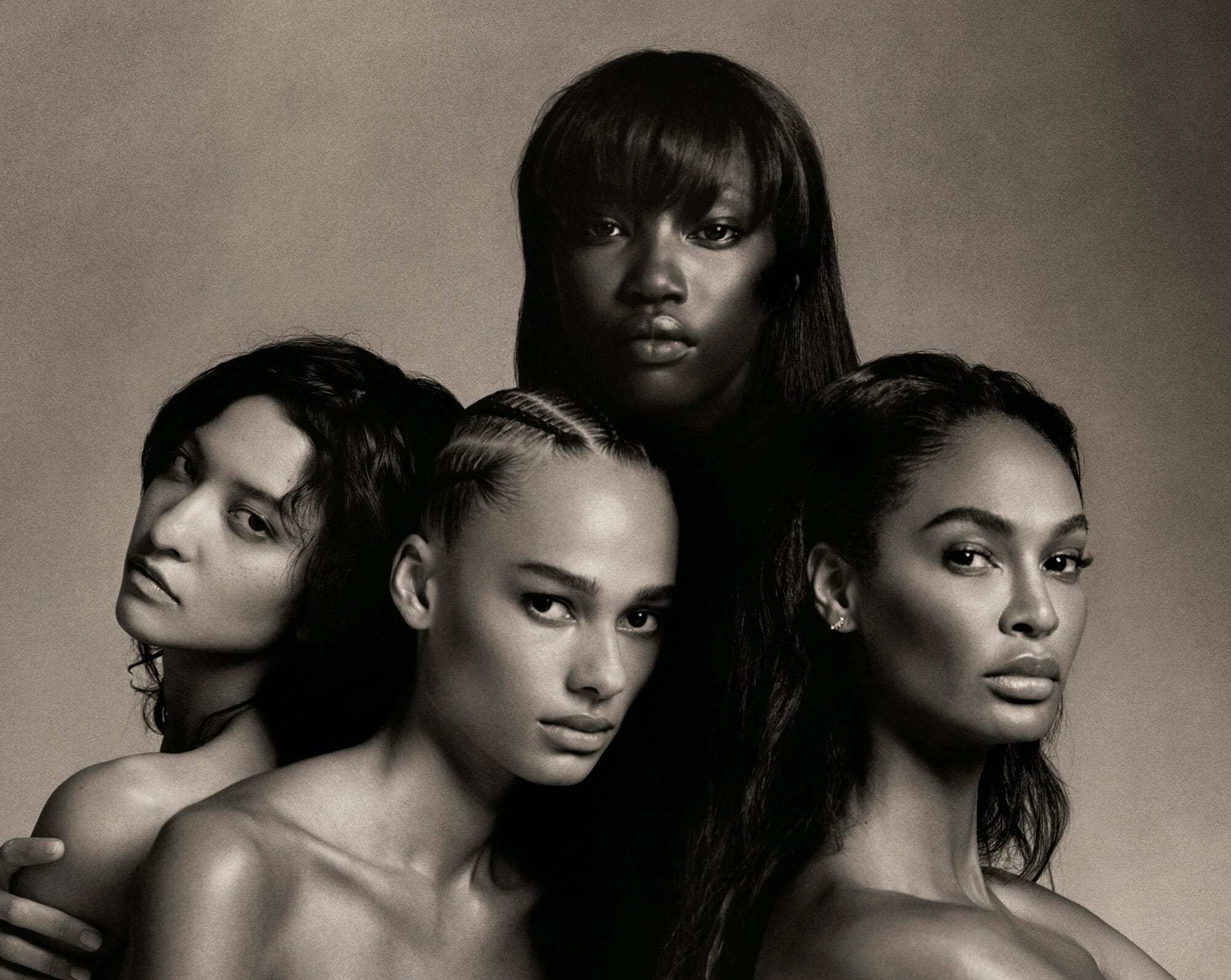 Black and white portrait of four diverse, topless women with various hairstyles looking directly at the camera in a photo studio setting.