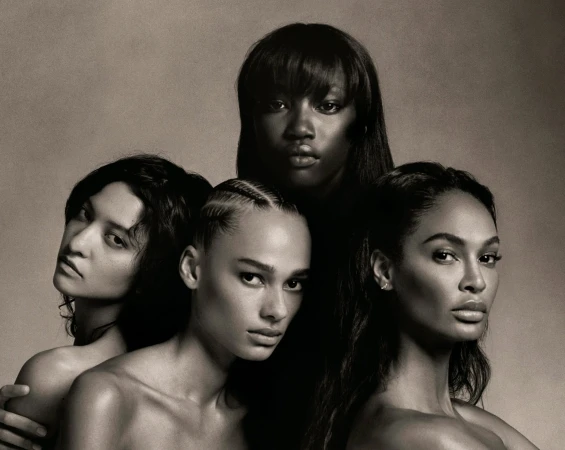 Black and white portrait of four diverse, topless women with various hairstyles looking directly at the camera in a photo studio setting.