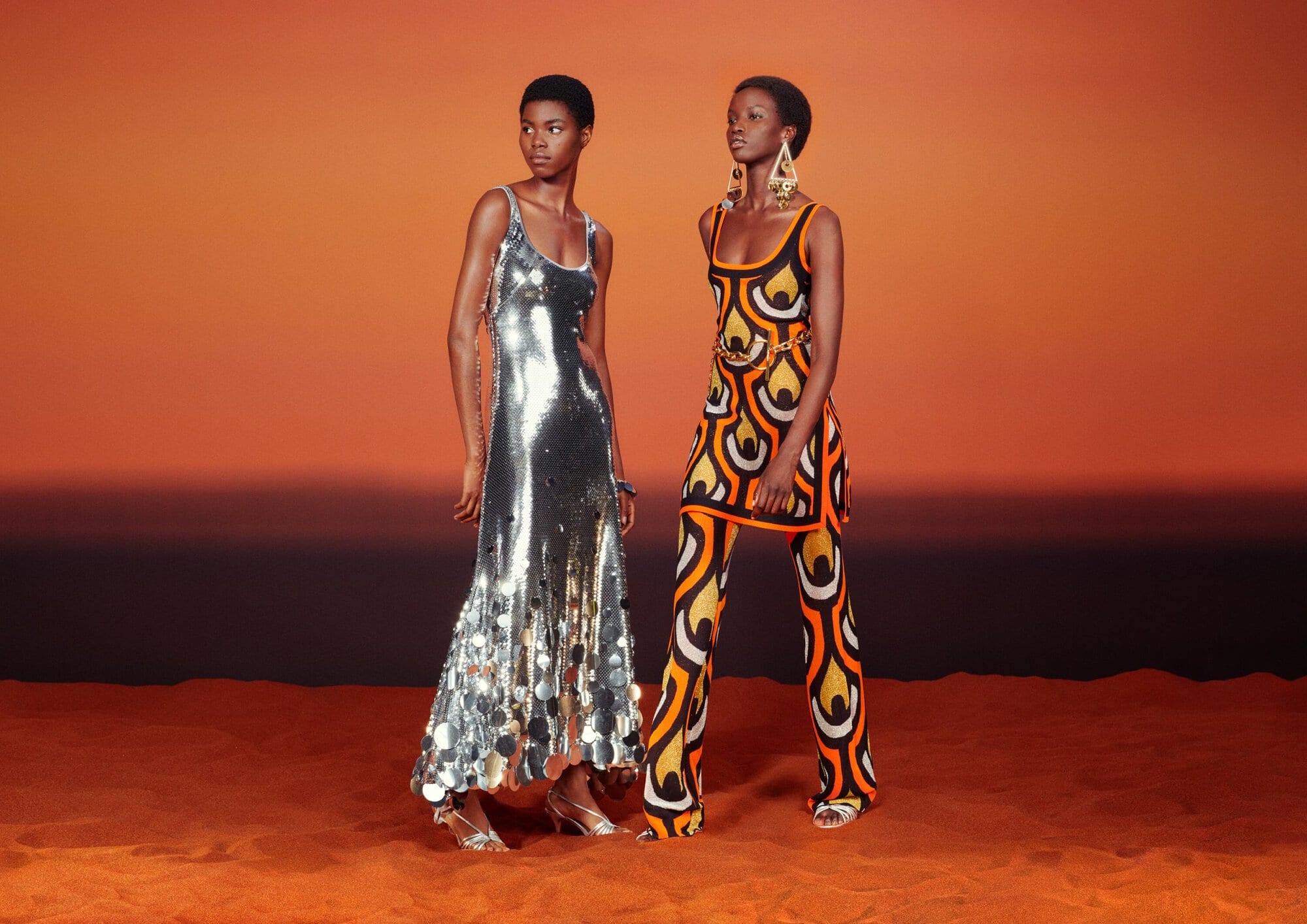 Two models standing in a desert at sunset wearing a silver sequin maxi dress and a retro geometric orange and black patterned outfit.