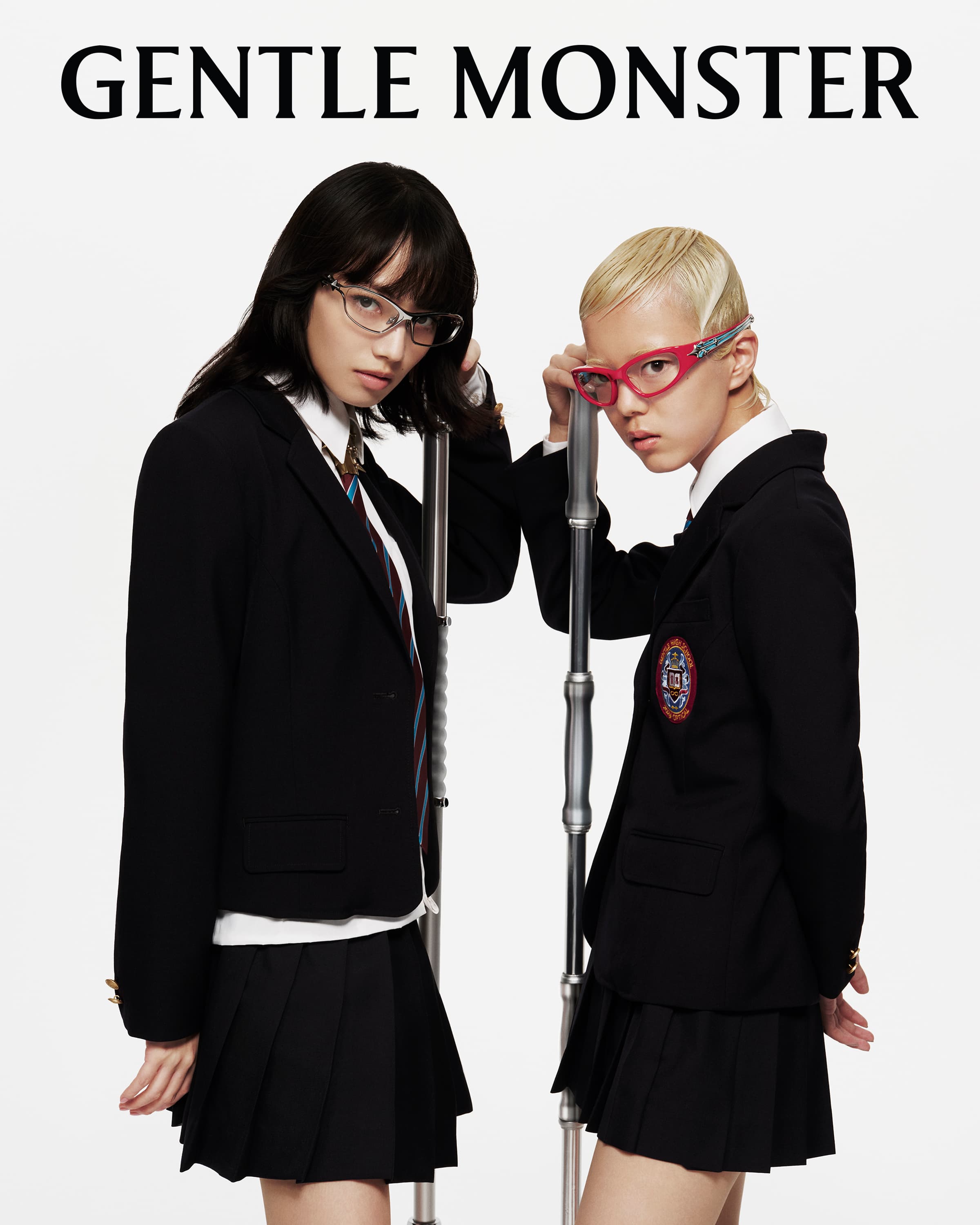 Two women model Gentle Monster eyewear in a studio setting. One has black hair and clear frames, the other has a shaved head and pink frames.