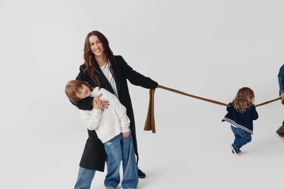 A happy mother smiles while holding a rope with her children, a son and a daughter, in a studio setting against a clean, bright white backdrop.