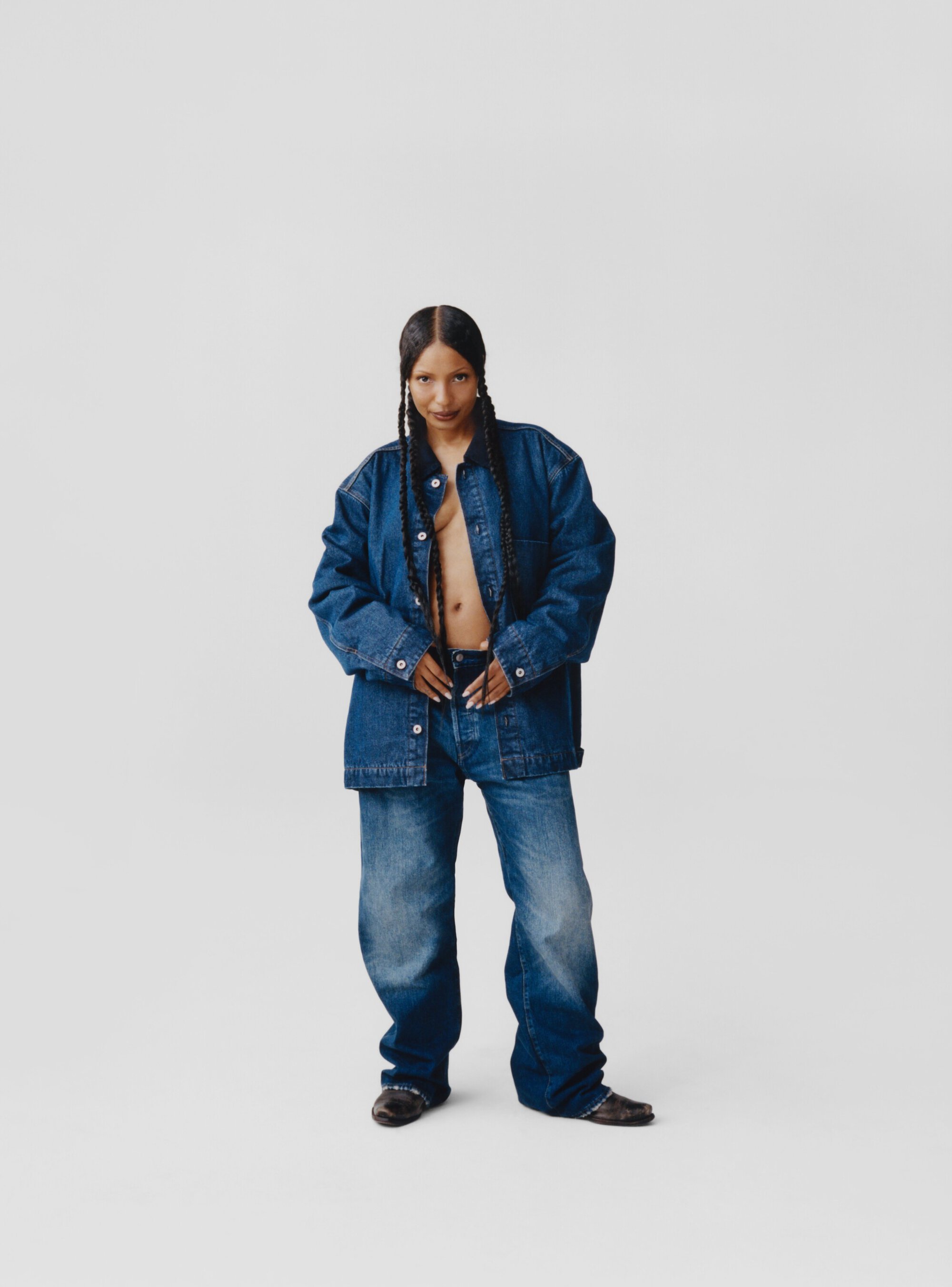 Full-length studio shot of an adult female wearing a denim jacket and jeans, looking at the camera against a plain white backdrop.