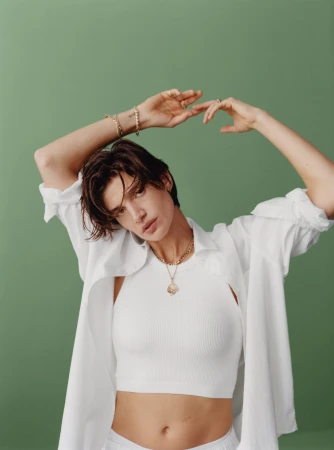 Model in white crop top and unbuttoned white shirt posing against a solid green background for Gap Holiday 2023