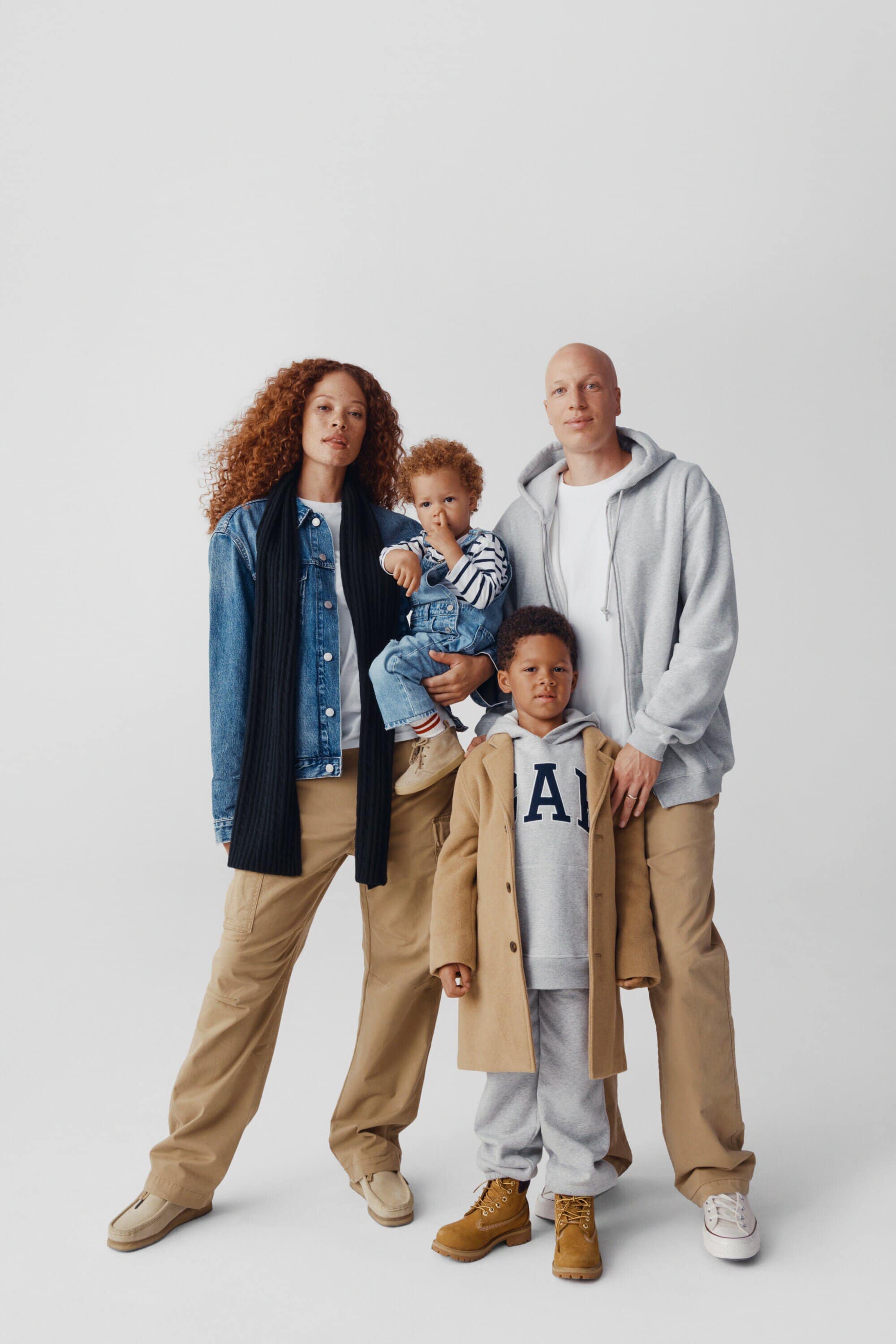 Family of four poses in a photo studio. The adults and children wear casual clothing in neutral tones. A young boy is held by the mother.