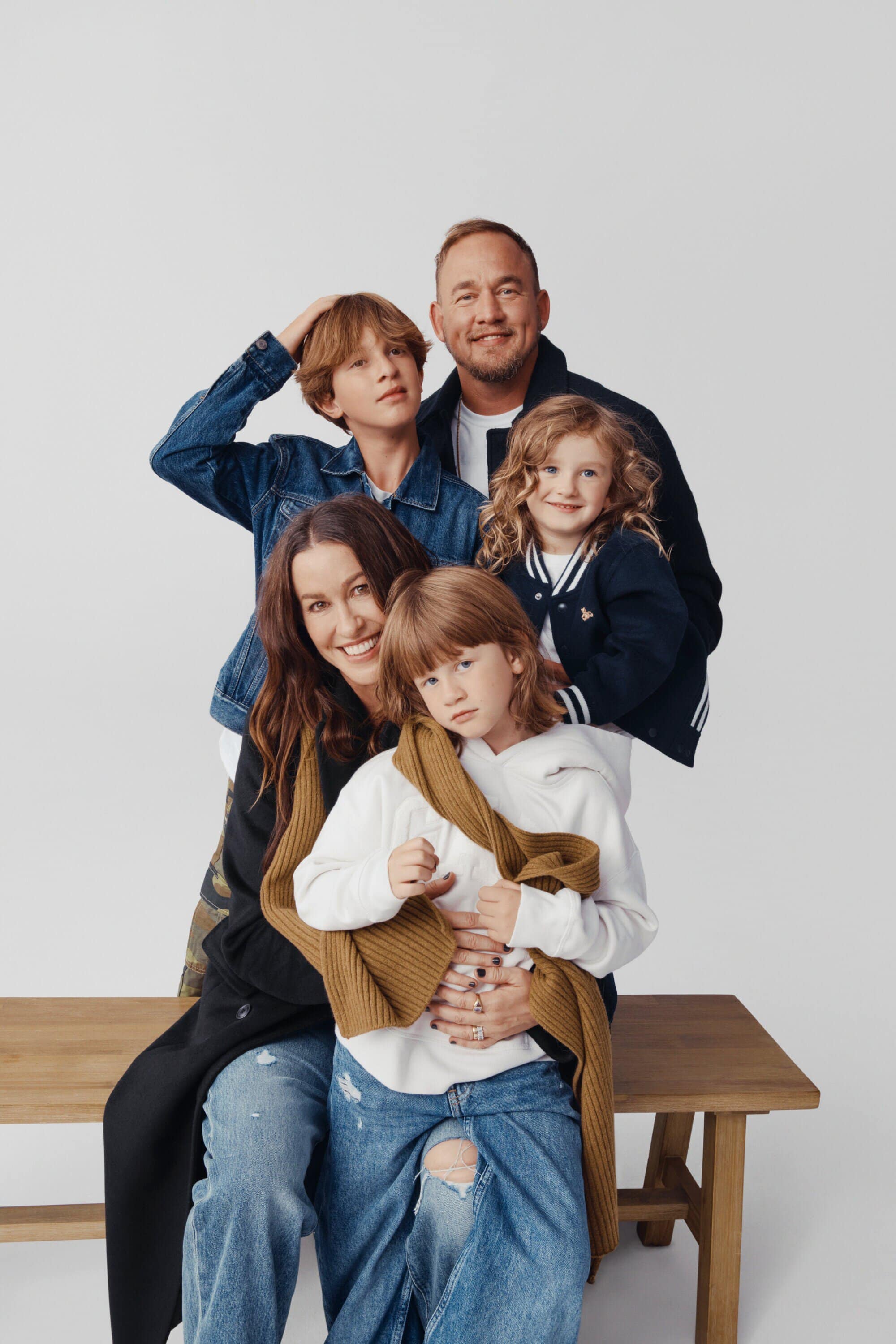Family portrait in a photo studio. The group of five people are smiling and posing in casual outfits against a white backdrop.