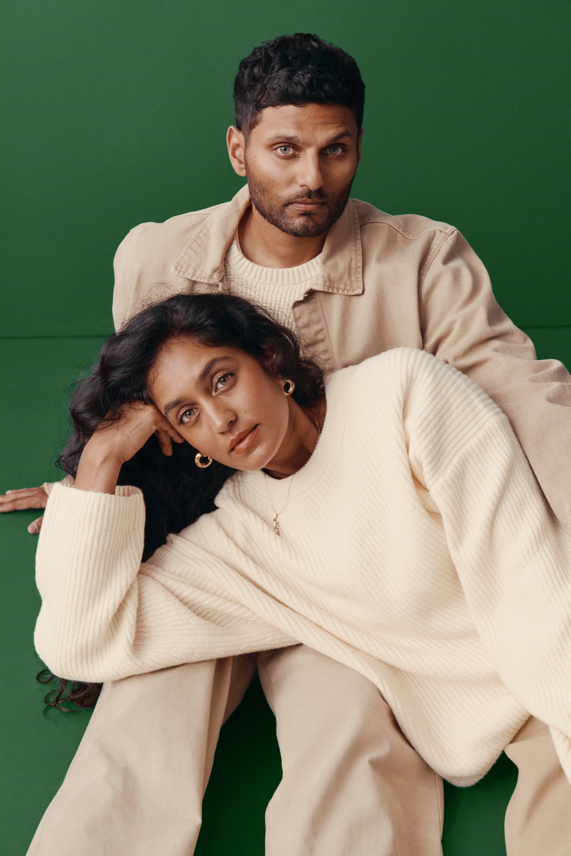 Portrait of a man and woman in neutral clothing against a green background, showcasing fashion and lifestyle elements.