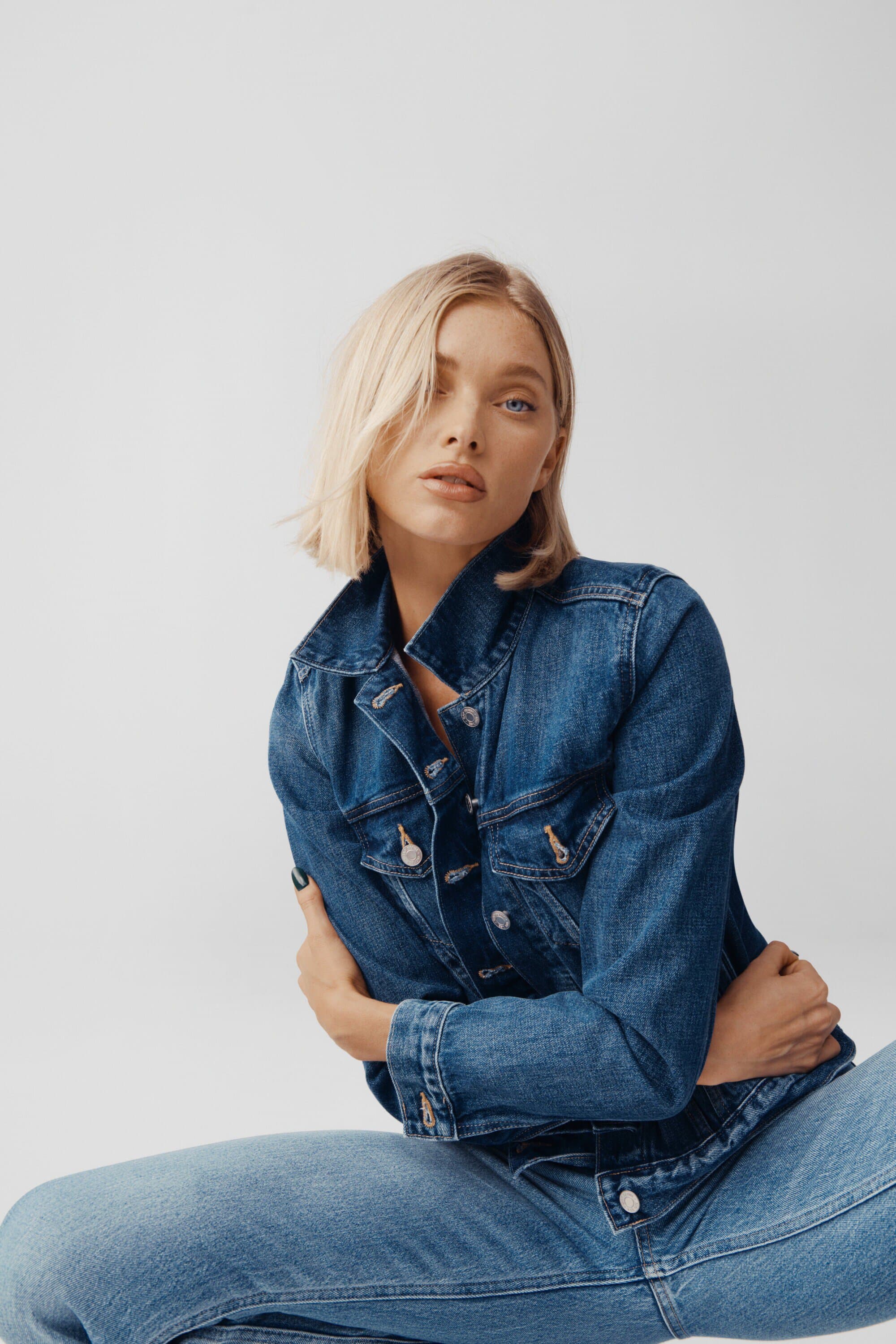 Model Elsa Hosk posing in a blue denim jacket and matching jeans against a white studio background.