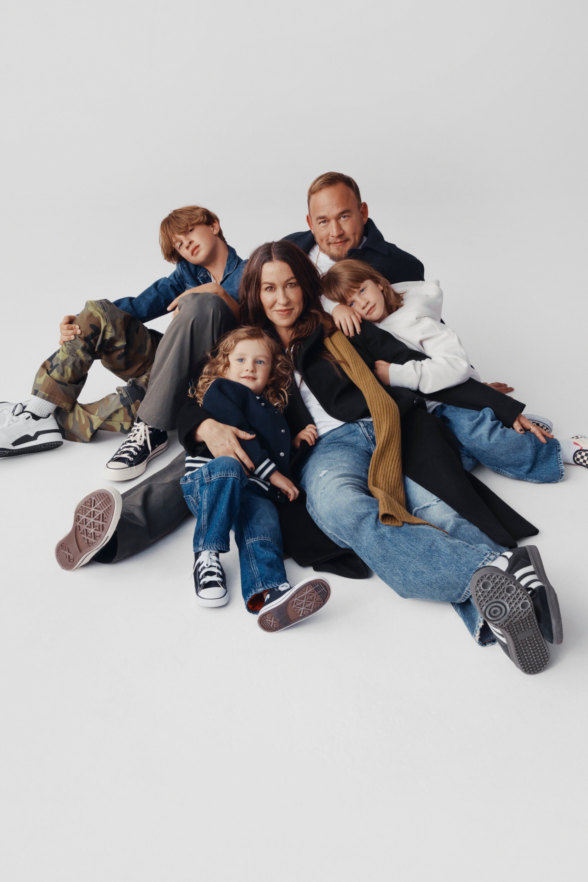 A family of five, including two adults and three children, poses together on a white backdrop, all dressed in casual clothing.