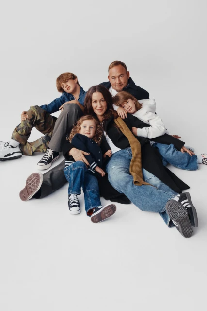 A family of five, including two adults and three children, poses together on a white backdrop, all dressed in casual clothing.