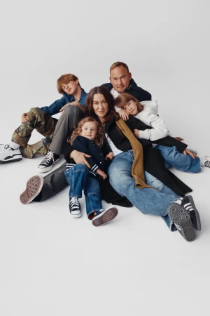 A family of five, including two adults and three children, poses together on a white backdrop, all dressed in casual clothing.