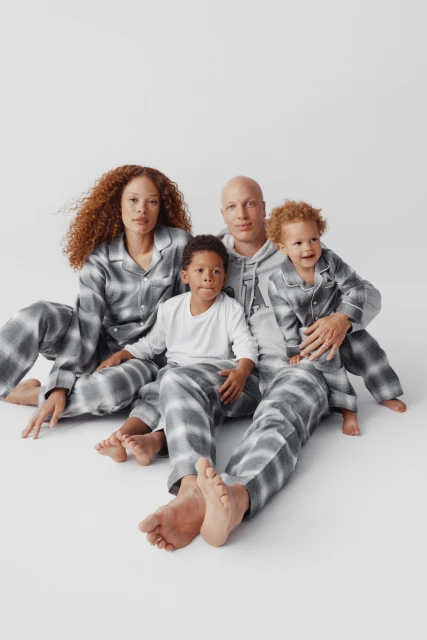 Family of four poses in matching grey patterned pajamas against a white backdrop. Two adults and two children, indoor setting, pajamas.