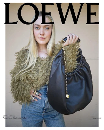 Dakota Fanning holding a black leather Loewe Squeeze bag wearing an olive textured sweater and blue jeans.