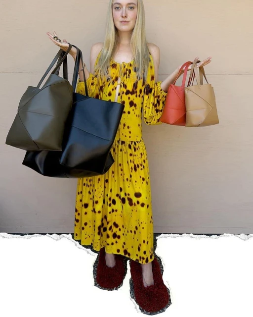 Blonde woman in a yellow dress holds two black and one tan tote bags, posing against a neutral background. She wears fuzzy, unique shoes.