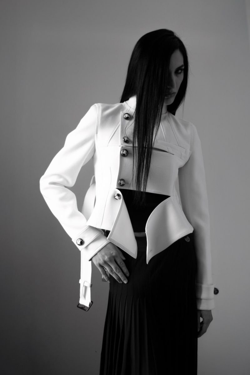 Monochrome fashion shot of a woman in a white jacket and black skirt posing against a gray backdrop with long black hair.