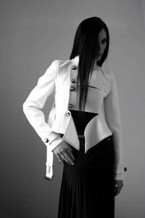 Monochrome fashion shot of a woman in a white jacket and black skirt posing against a gray backdrop with long black hair.