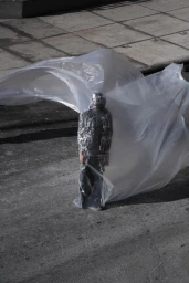 Model wrapped in flowing transparent plastic sheeting standing on a grey concrete surface photographed by Joaquin Castillo for METAL Magazine.