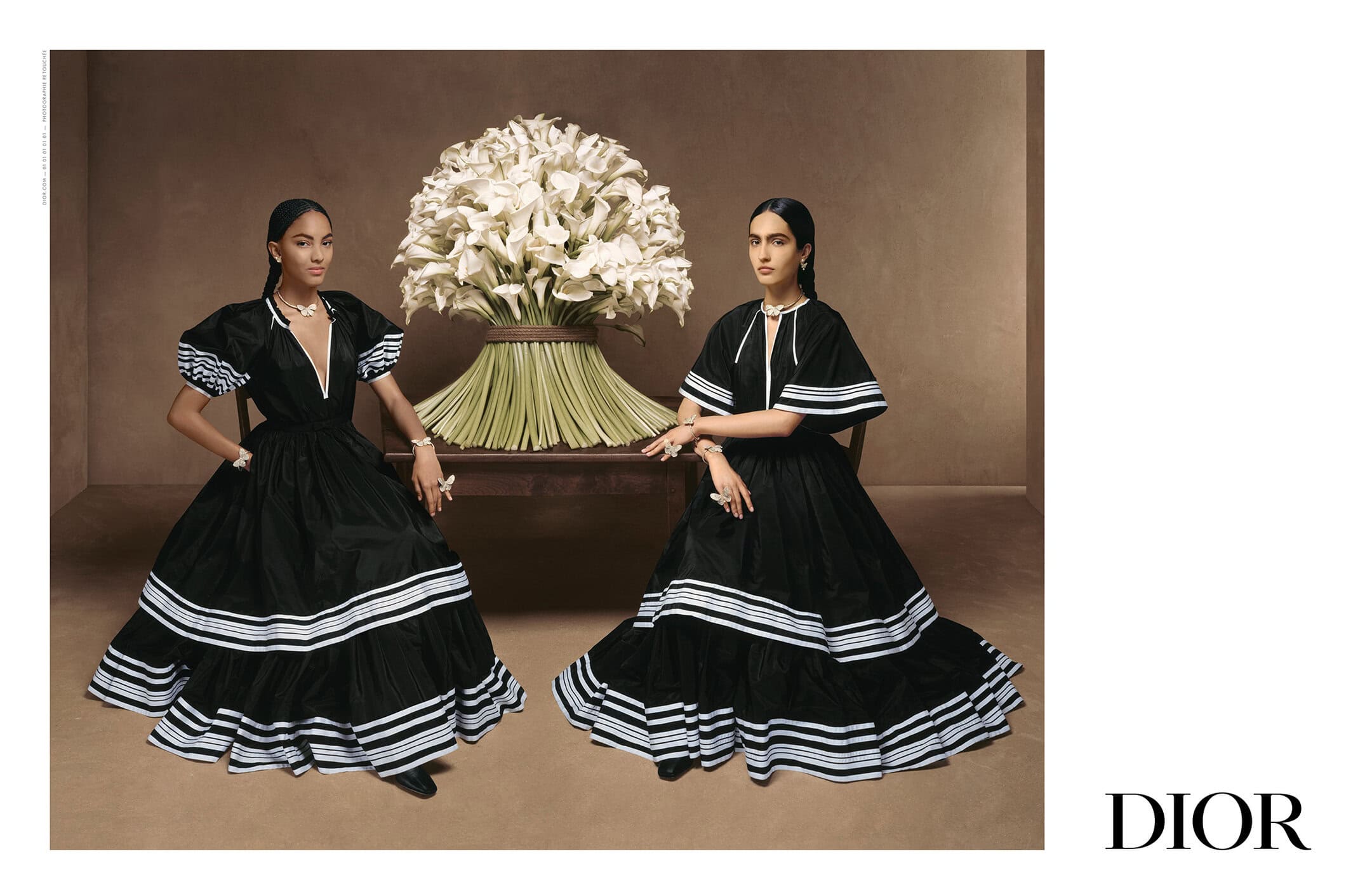Two women in black dresses pose near a bouquet of calla lilies in a studio setting, exuding elegance and classic fashion.