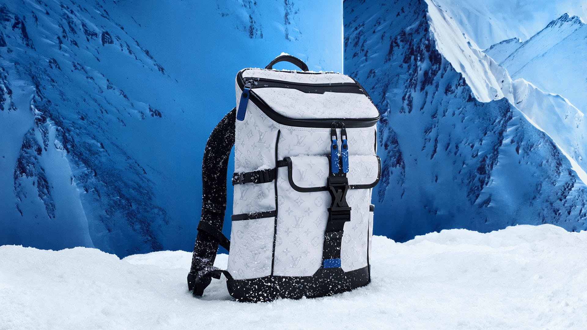 White Louis Vuitton backpack sits on a snowy surface in front of a snowy mountain range in an outdoor, daytime product shot.