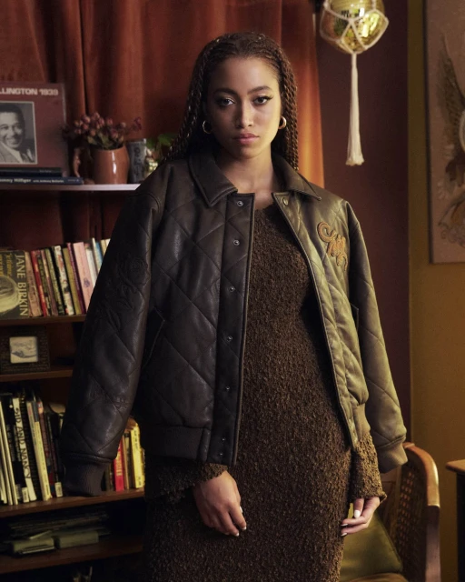 Woman in brown leather jacket and knitted dress poses indoors near a bookshelf with warm, natural lighting and a nostalgic aesthetic.