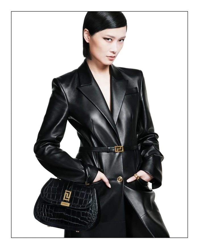 Asian woman wearing a black leather coat and holding a black handbag against a bright white background
