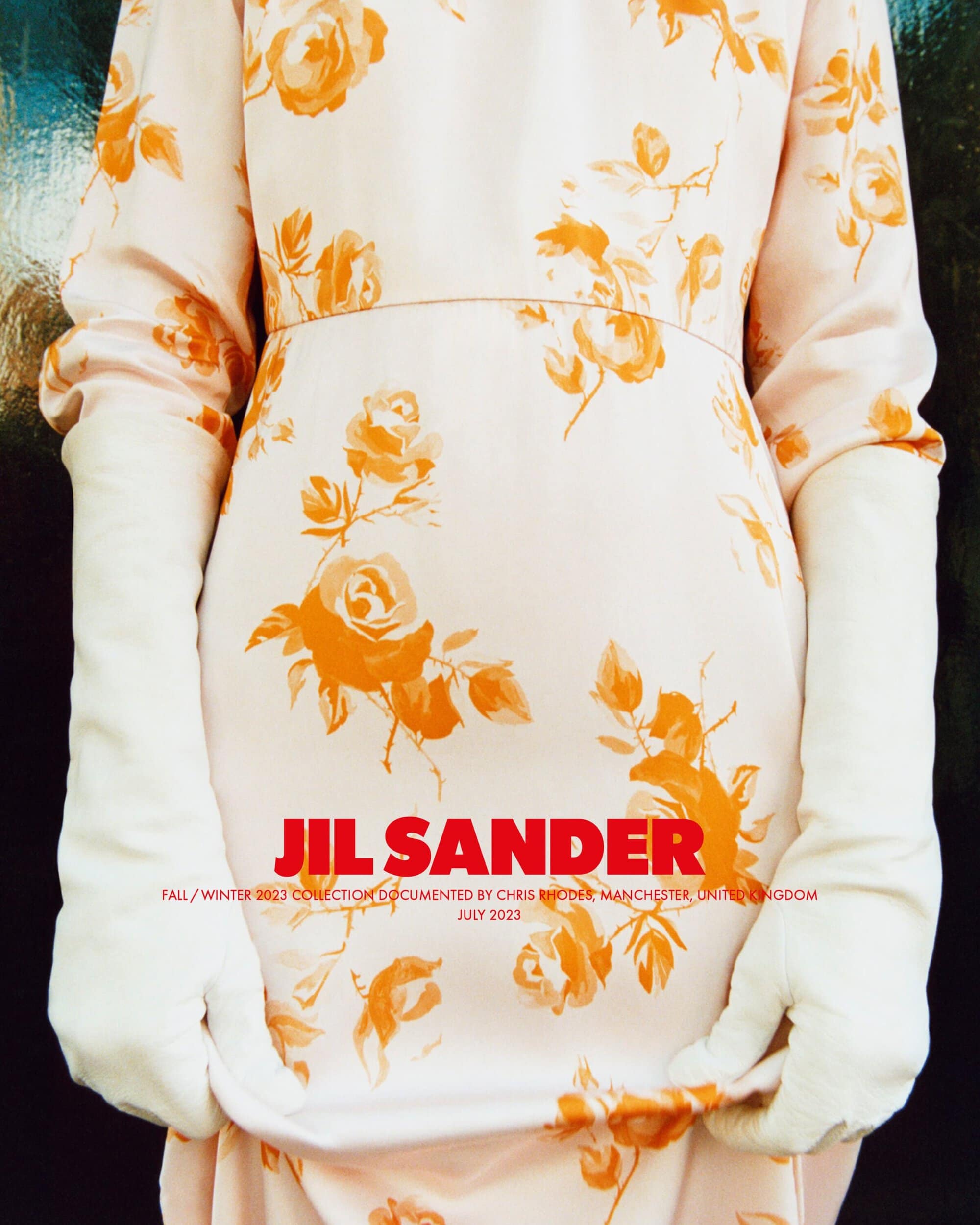 A model showcases a Jil Sander floral dress with white gloves, captured indoors in a fashion editorial with a shallow depth of field.