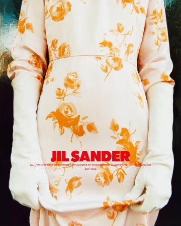 A model showcases a Jil Sander floral dress with white gloves, captured indoors in a fashion editorial with a shallow depth of field.