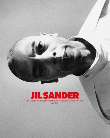 Close-up black and white portrait of a bald adult male wearing a white shirt, angled slightly downward, with Jil Sander text overlay.