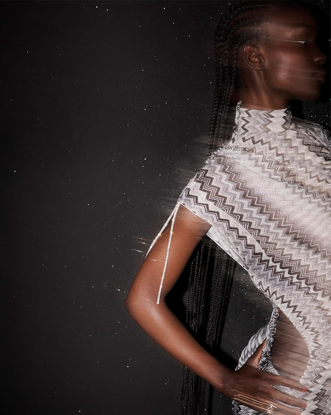 A striking fashion portrait of a woman with dark skin and braided hair, wearing a patterned mock-neck dress against a dark background.