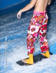 Shirtless person wearing floral print pants and yellow socks on a surfboard riding a wave