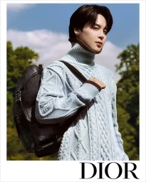 Jimin wearing a light blue cable knit turtleneck sweater and carrying a dark leather backpack against an outdoor backdrop