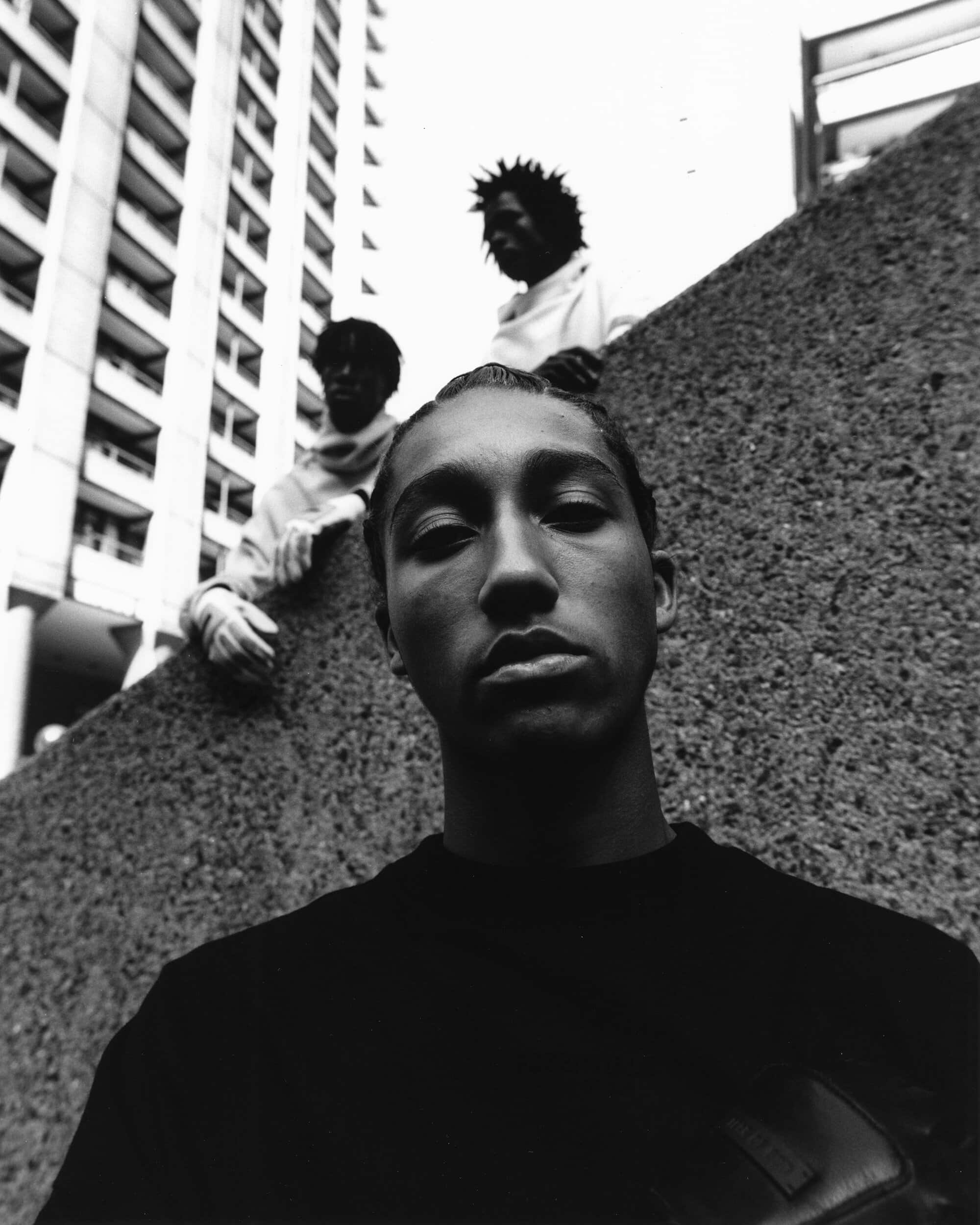 Black and white eye-level shot of three men outside a high-rise building, one in the foreground and two in the background.