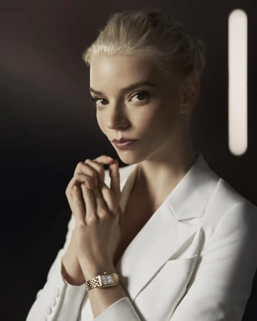 Anya Taylor-Joy portrait: blonde hair, white suit, gold watch against a dark background with diffused lighting. Beauty and fashion shot.