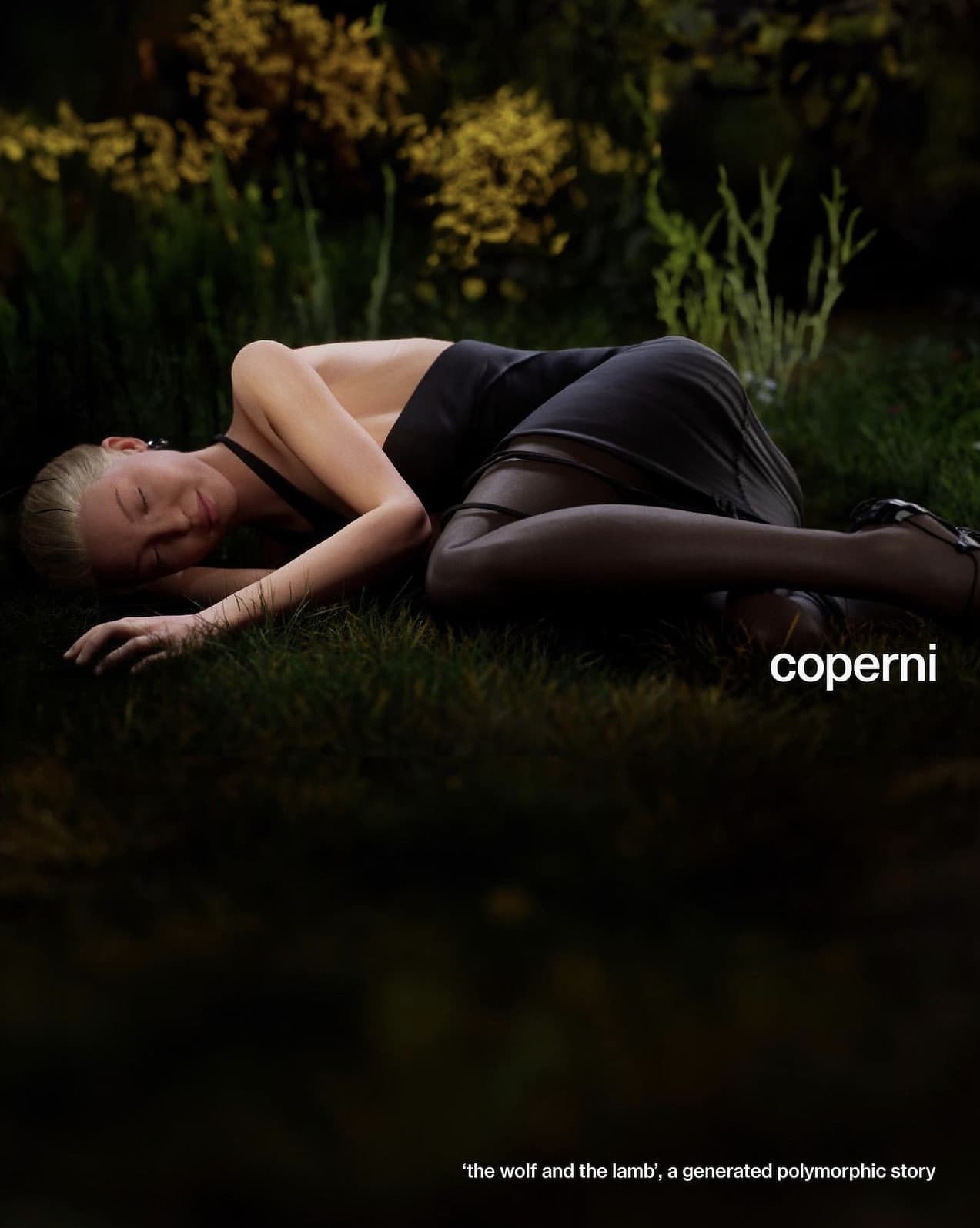 A fair-skinned woman with blond hair lying on a grass surface in a dark, outdoor setting wearing a black dress and black high heels.