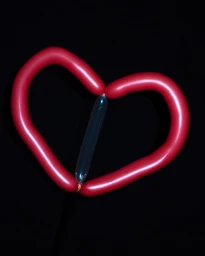 A red heart-shaped twisted balloon sculpture with a clear vertical tube balloon in the center against a solid black background.