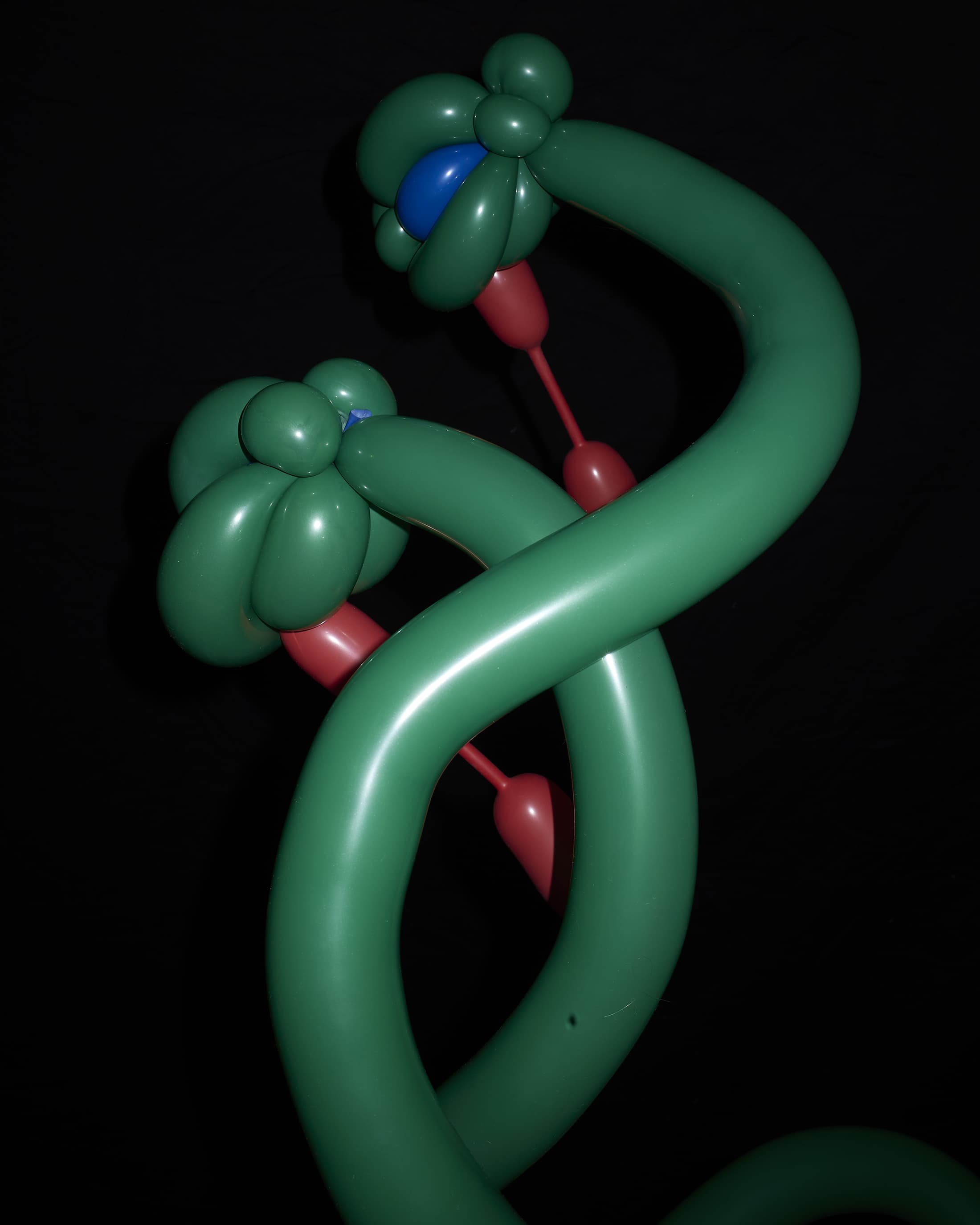 Two green balloon sculptures with flower-shaped heads, red stems, and a blue center stand against a dark background, showcasing balloon art.