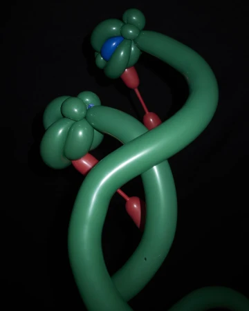 Two green balloon sculptures with flower-shaped heads, red stems, and a blue center stand against a dark background, showcasing balloon art.
