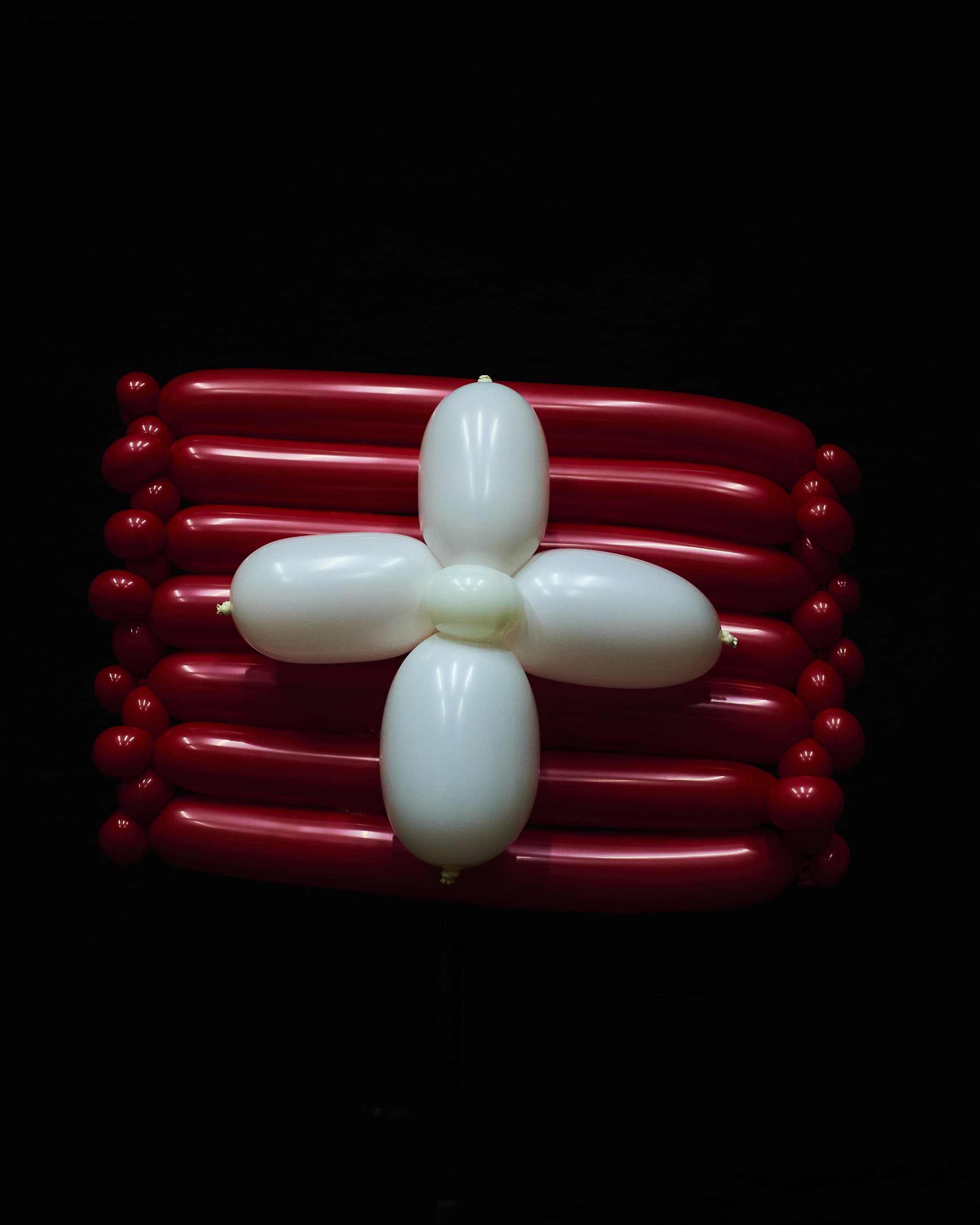 Balloon art rendering of the Swiss flag: a white cross centered on a red rectangular background, isolated on black.