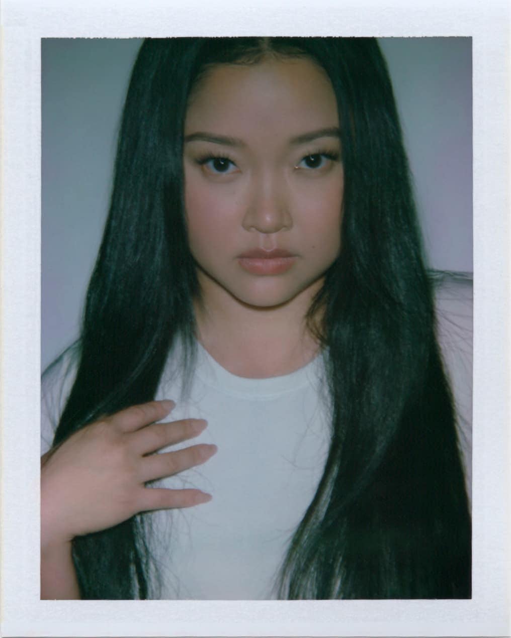 Portrait of a young adult woman with long, dark hair and a light complexion, posing in a white t-shirt against a plain background.