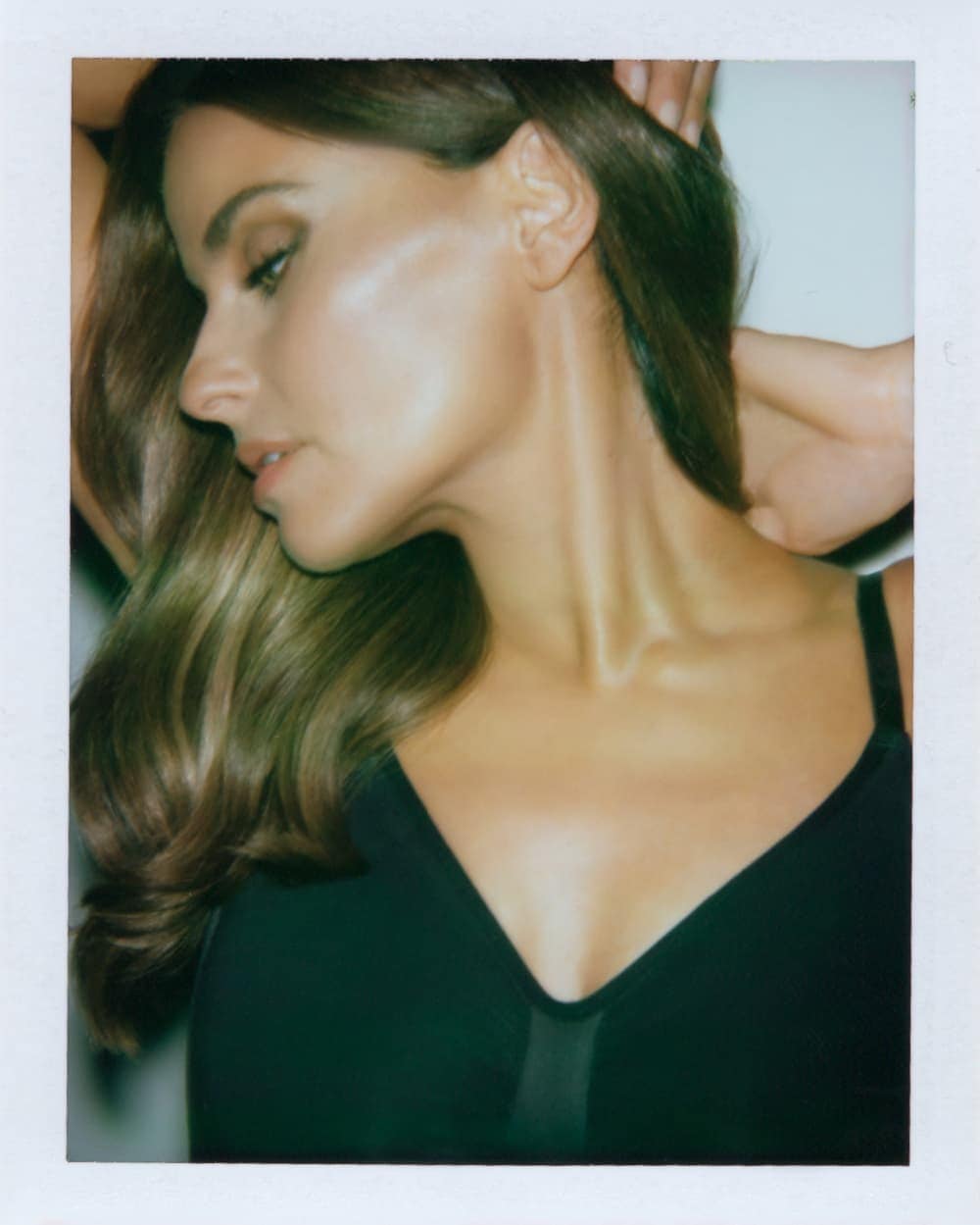 Close-up portrait of an adult woman with long brown hair, wearing a black top, against a plain white background in a studio setting.