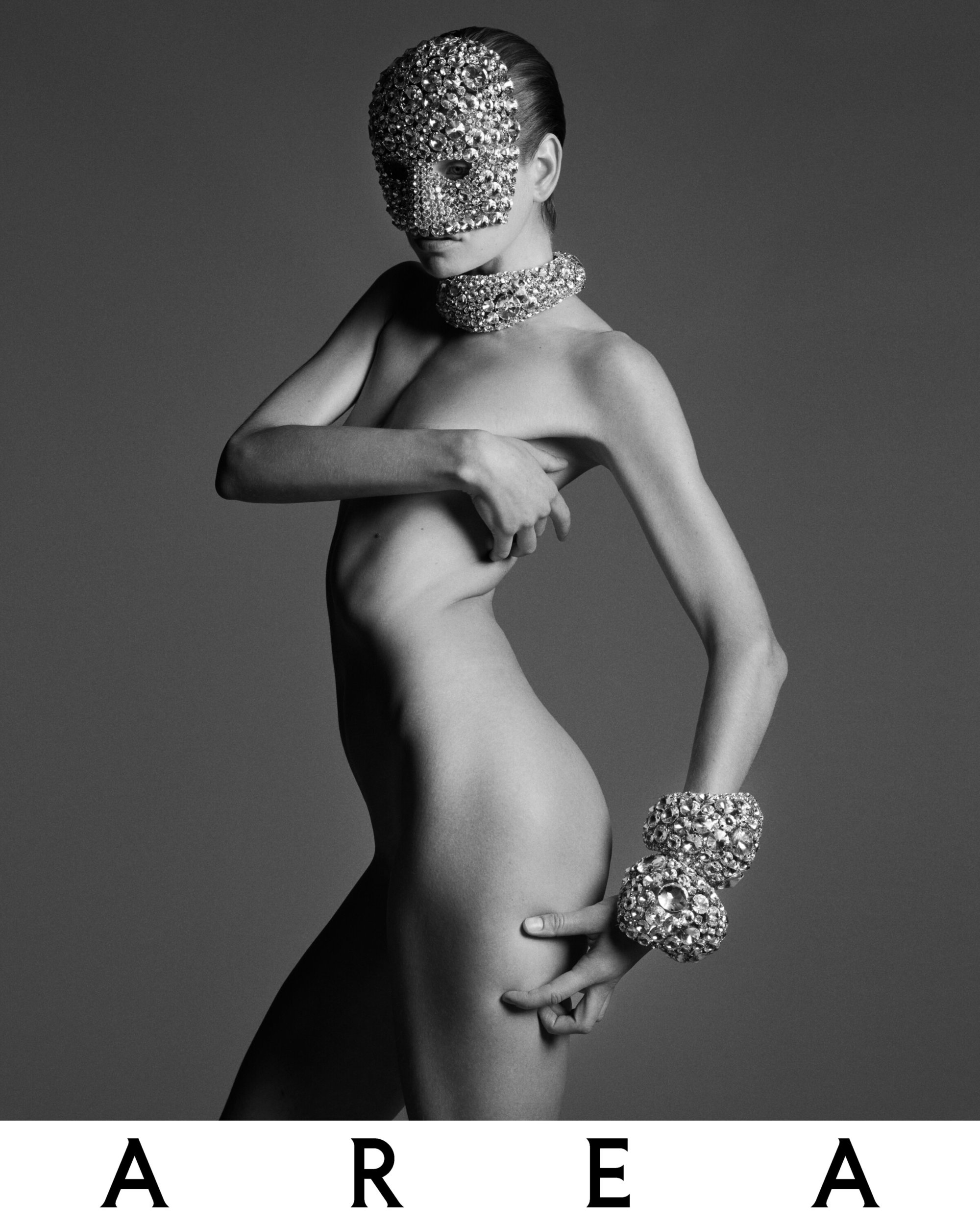 Model Sylvia Anderson wearing a sparkling crystal face mask and matching jewelry against a grey studio backdrop for Area.